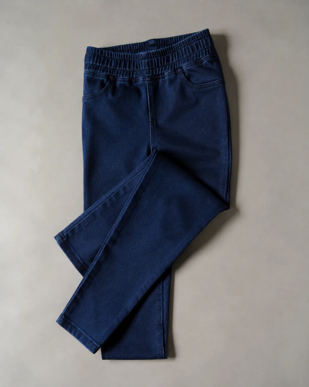 a pair of jeggings laid flat with one leg folded back across the other with a full elastic waistband , fabric: Cotton, rayon, polyester and Lycra spandex (percentages not published)
